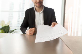 Smiling job applicant in suit handing over resume to recruiter during interview. Modern office setting. Recruitment manager giving resume back to candidate. Human resources, hiring, interview concept.