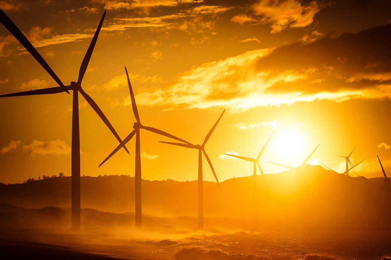 Wind turbine power generators silhouettes at ocean coastline at sunset. Alternative renewable energy production in Philippines